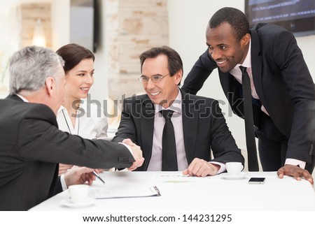 Business colleagues sitting at a table during a meeting with two male executives shaking hands