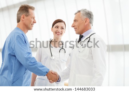 Welcome on board! Two mature doctors handshaking while  beautiful young nurse looking at them