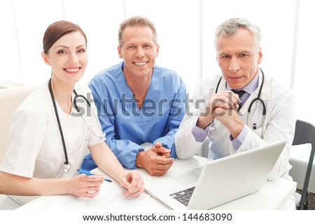 Medical team at work. Cheerful medical team sitting together at the table and looking at camera