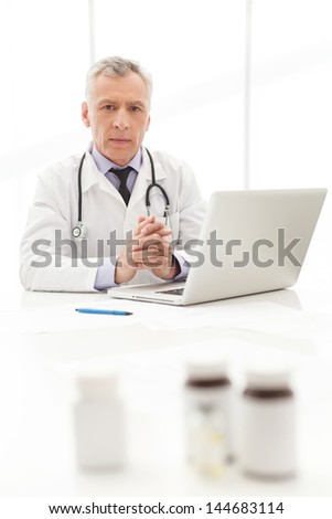 Medical doctor.Mature  doctor sitting at his working place with the medicines on the foreground