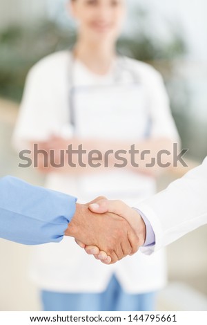 Welcome to the team. Close-up of male doctors handshaking while female doctor smiling on the background
