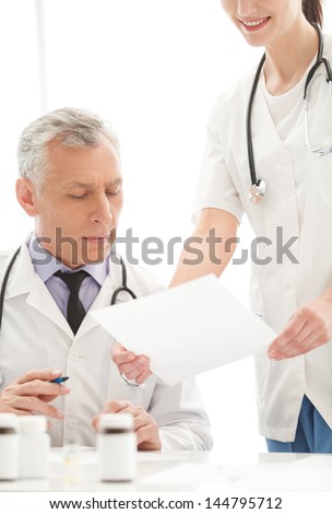 The document to sign. Young cheerful female doctor holding a document to sign while standing near her mature colleague