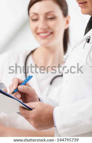 Going through a report. Close-up of two medical doctors writing in the writing pad together