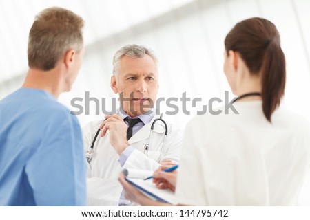 Caring team of medical healthcare professionals. Three doctors discussing the report standing close to each other