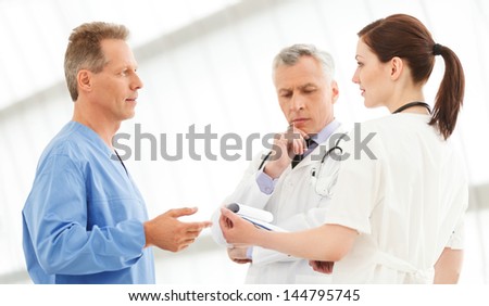Figuring out the correct medication. Three doctors discussing the report standing close to each other