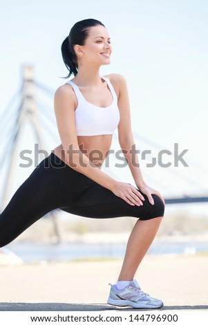 Good place for exercising. Beautiful woman doing her outdoor exercises with a bridge on the background