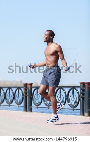 Man jumping on the jumping rope. Young african descent men with naked torso jumping on the jumping rope outdoors
