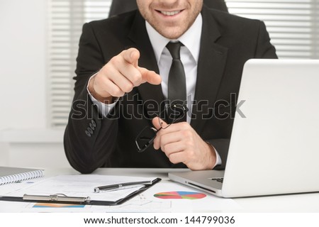 Businessman sitting at the table Pointing at the Camera smiling ans showing confidence