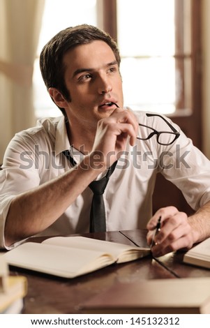 Waiting for inspiration to strike. Handsome young author sitting at the table with a pen in his hand and waiting for inspiration