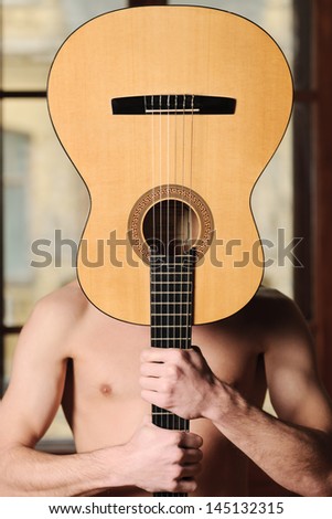 Music is everything for him. Naked men holding an acoustic guitar in front of his head