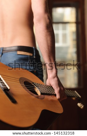 My guitar is always with me. Rear view of men with naked torso holding an acoustic guitar in his hand