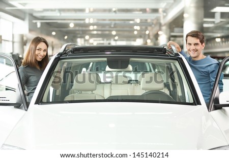 Happy with their new car. Happy young couple standing at both sides of the car smiling at camera