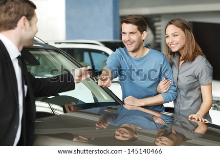 They have made a right vehical choise. Young car salesman giving a key from the new car to the beautiful young owners