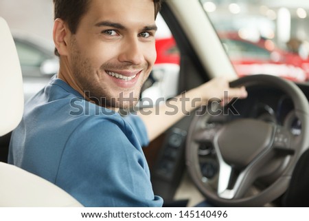 Happy car owner at the dealership. Handsome young men sitting at front seat of the car looking at camera