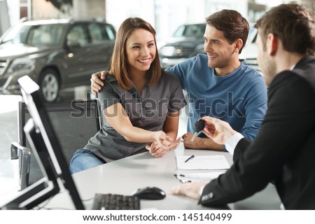 Now Her Dream Comes True. Car Salesman Giving The Key Of The New Car To The Young Attractive Owners