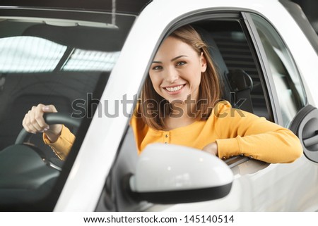 She has bought her dream car! Attractive young woman sitting at the front seat of the car looking at camera