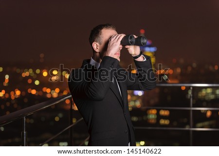 Businessman looking through binoculars to see what he can find on background night city