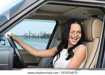 An attractive young Caucasian woman winking at the camera from the front seat of the car