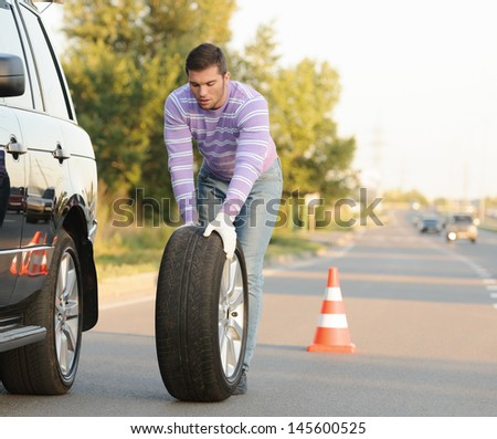 Handsome young man rolling a spare wheel using gloves