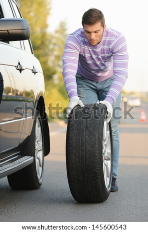 Handsome young man rolling a spare wheel using gloves