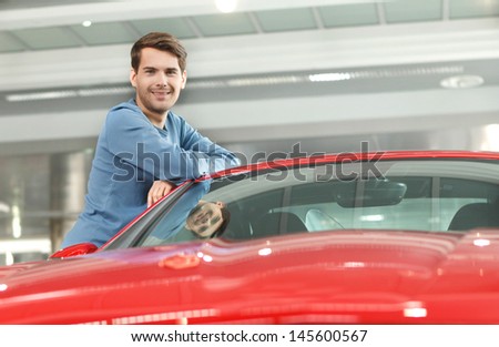 Happy car ownner. Handsome young men leaning on his new car at the dealership
