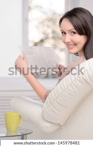 Only good news. Beautiful middle-aged woman sitting on the couch reading a Sunday paper