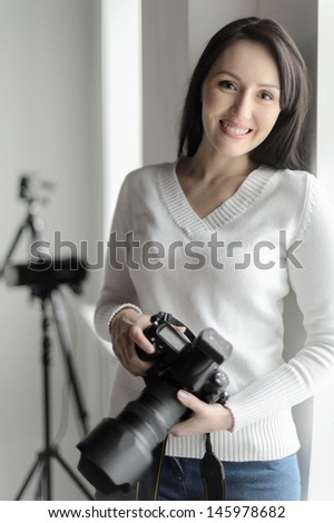 Photography is her hobby. Beautiful middle-aged woman standing in the studio and holding camera