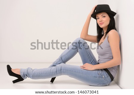 In style. Beautiful young woman doing sitting on the floor and holding her hand on her hat