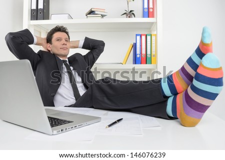 Businessman in funky socks. Confident businessman holding his legs in funny socks on the desk