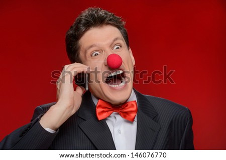 He is not taken seriously. Portrait of angry man with a clown nose touching talking at phone and shouting