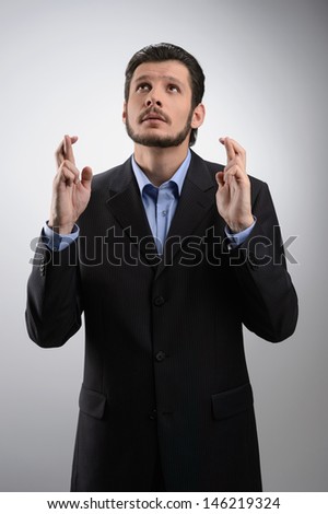 Keeping his fingers crossed. Businessman standing with his fingers crossed against grey background