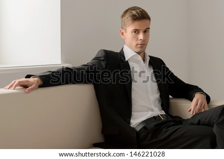 Confident young men. Handsome young men in formalwear sitting on the couch and looking at camera