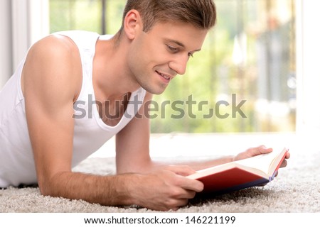 Exciting book.  Side view of handsome young men reading a book while lying on the floor