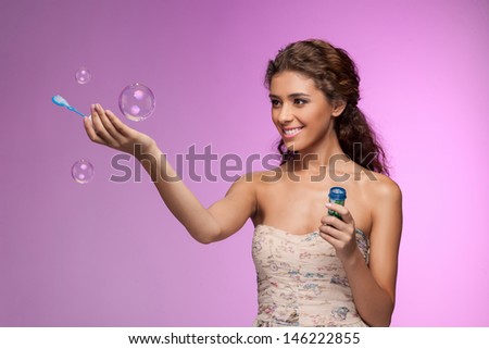 Playing with a bubble wand. Beautiful young women playing with the soap  bubbles while standing isolated on colored background