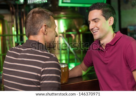 Friends having fun at bar. Two cheerful male friends talking at bar and drinking beer