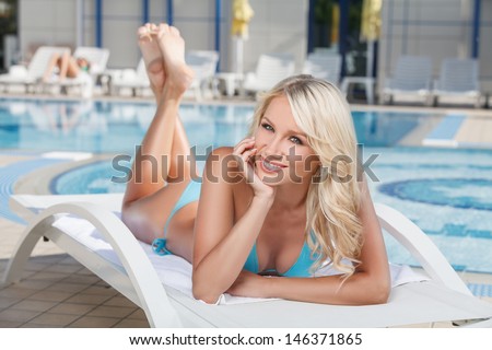 Summer beauty. Cheerful young women in bikini lying on the deck chair near the pool and holding her head in hand