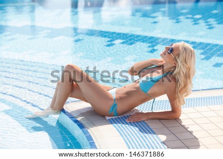 Women on poolside. Side view of attractive young women in bikini lying on the poolside