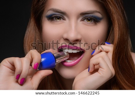 I choose the blue one! Portrait of beautiful women holding a nail polish in her teeth