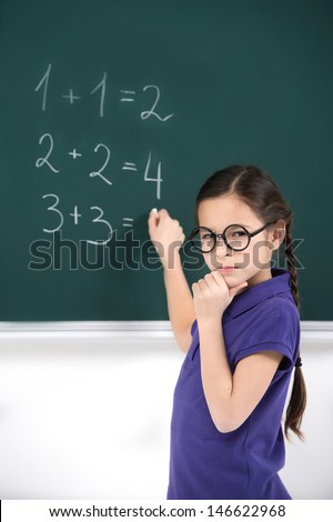 She knows the answer. Confident little schoolgirl thinking about the right answer near the blackboard
