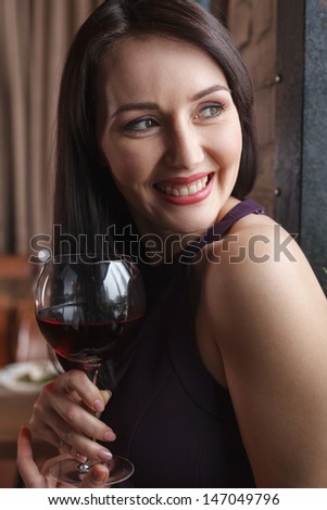 Smiling to him. Beautiful middle-aged women standing with a glass of wine and looking away