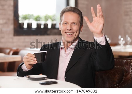 Happy businessman at restaurant. Cheerful businessman drinking coffee and gesturing while sitting at restaurant