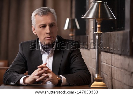 Businessman thinking about new ideas for business. Thoughtful mature businessman sitting with his fingers crossed and looking away