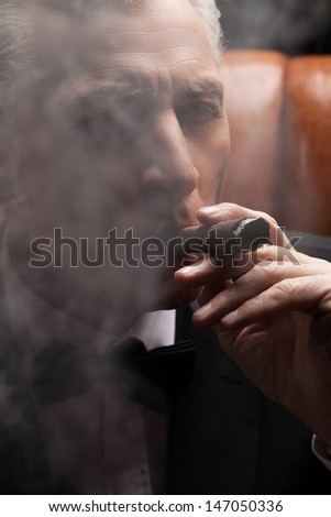 Through a cigar smoke. Close-up of confident mature man smoking a cigar