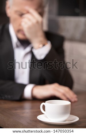 Depressed businessman. Depressed mature businessman sitting at the restaurant with his head in hand and the cup of coffee at the foreground