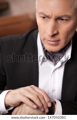 Worried businessman. Worried mature businessman checking the time and looking away
