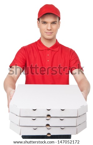 Here Is Your Pizza! Cheerful Young Deliveryman Stretching Out A Stack Of Pizza Boxes While Isolated On White