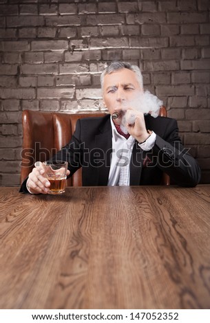 He is a boss. Bossy mature man in suit smoking a cigar and drinking whiskey