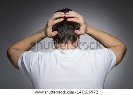 Men with headache. Rear view of men holding his head in hands while standing isolated on grey