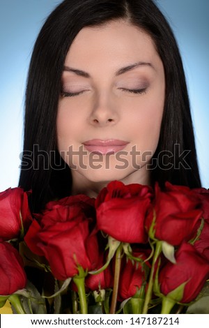 Women with red roses. Beautiful middle-aged women holding a bunch of red roses and keeping her yes closed while isolated on blue