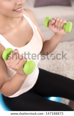 Sports at home. Top view of beautiful young women exercising at home while sitting on the fitness ball and using the dumbbells